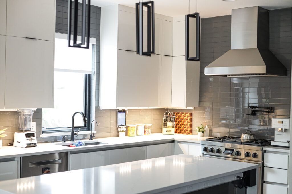 modern kitchen design with sleek white cabinets, black pendant lighting, a large island with a polished quartz countertop, and a stainless steel range hood.